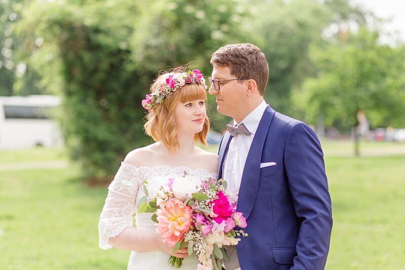 Brautpaar im Grünen mit Blumenkranz und großen pinken Blumen