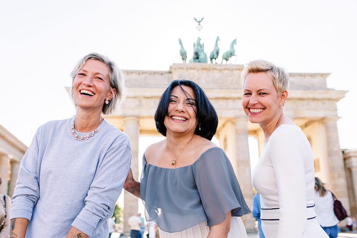 Drei Frauen lachen in die Kamera vor dem Brandenburger Tor Berlin