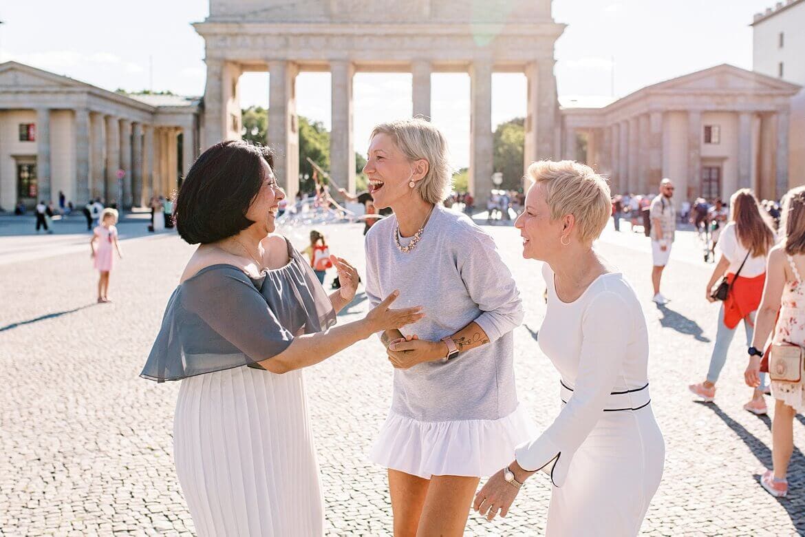 Drei Frauen schauen sich an und lachen vor dem Brandenburger Tor Berlin