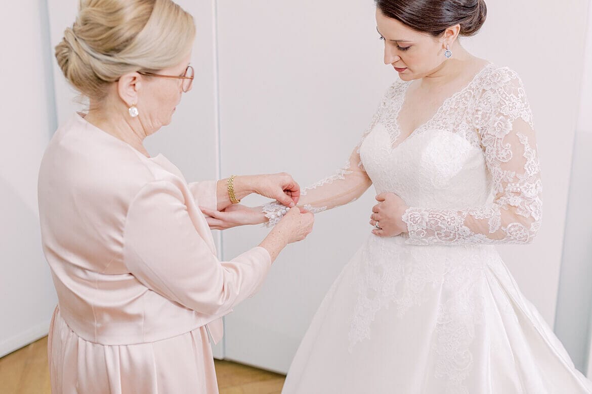 Brautmutter hilft Braut beim Anziehen des Brautkleids