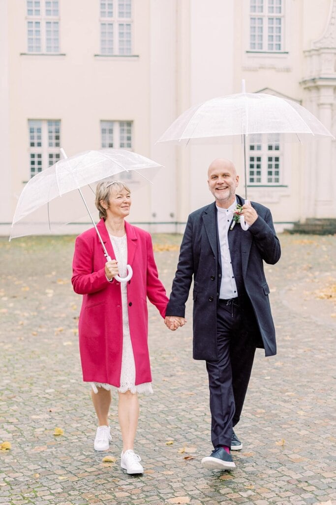 Brautpaar läuft unter Regenschirmen im Herbst vor dem Schloss Köpenick Berlin