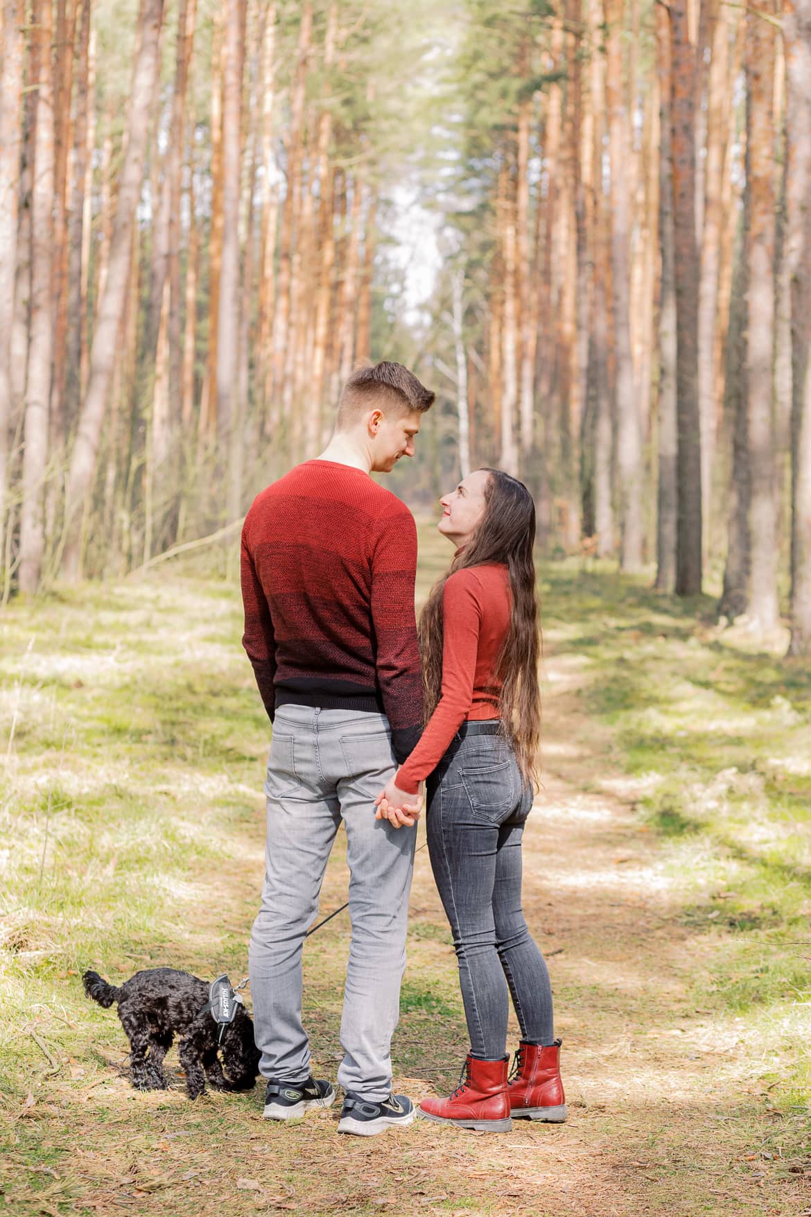 Pärchen mit Hund steht im Wald und schaut sich an