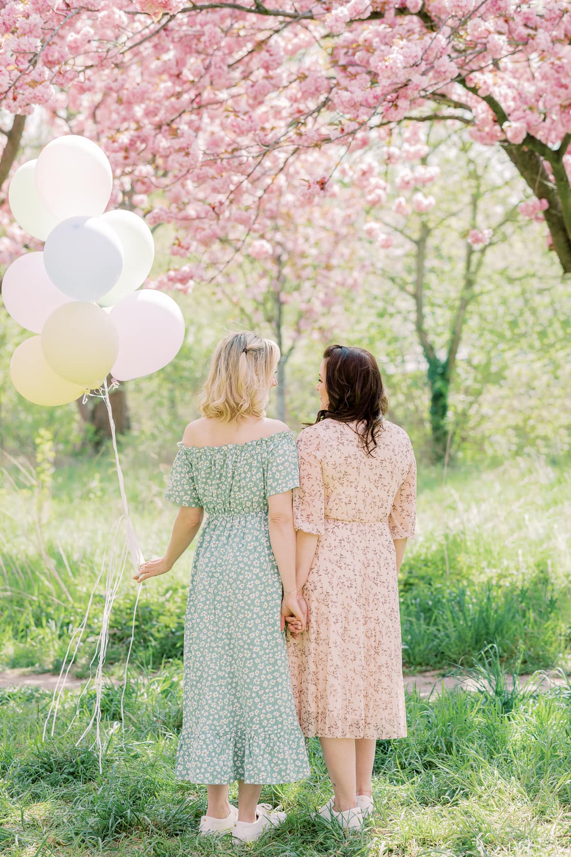 Zwei Freundinnen stehen mit dem Rücken zur Kamera und schauen sich an, eine hat Luftballons in der Hand