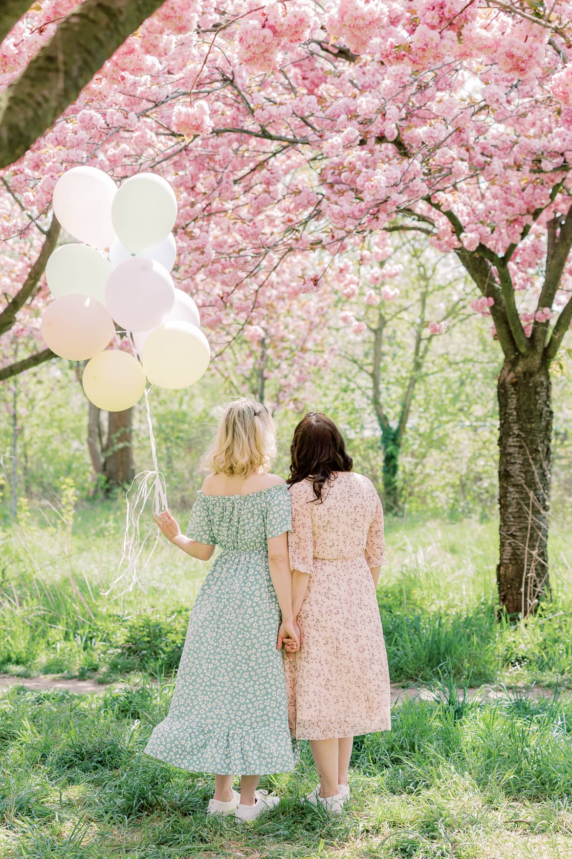 Freundinnen stehen mit dem Rücken zur Kamera, eine hat Luftballons in der Hand