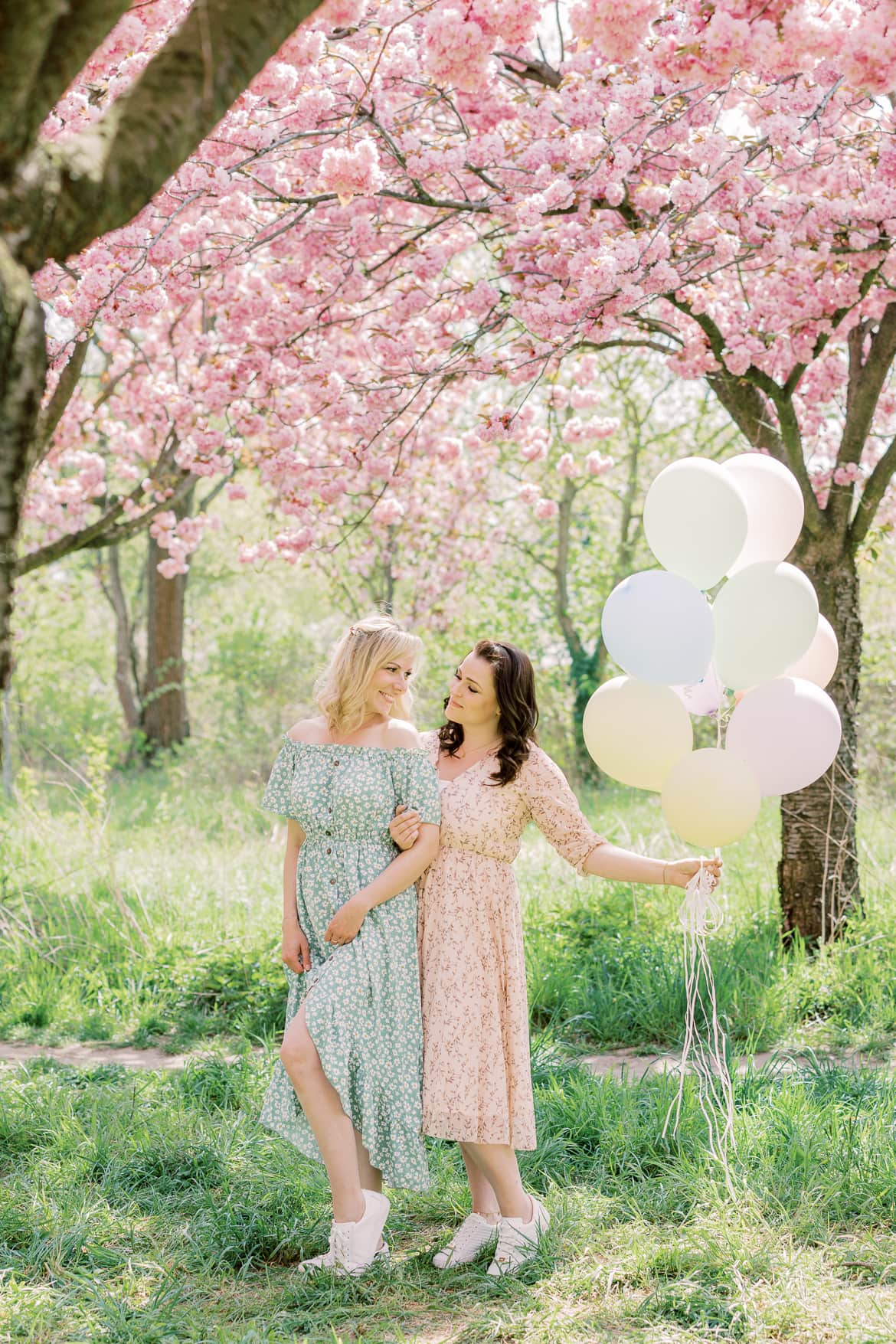 Zwei Freundinnen stehen mit Luftballons unter Kirschblüten