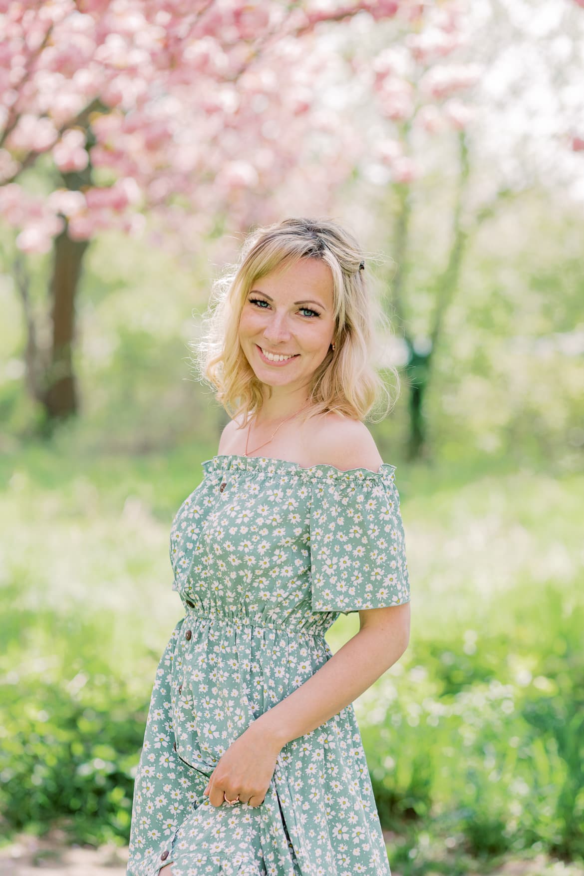 Eine blonde Frau im grünen Blumenkleid unter Kirschbäumen