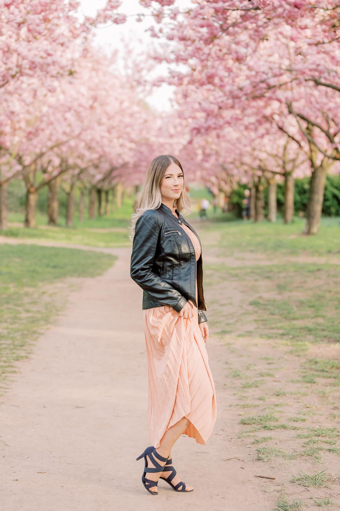 Eine Frau im Abendkleid und Lederjacke unter Kirschblüten