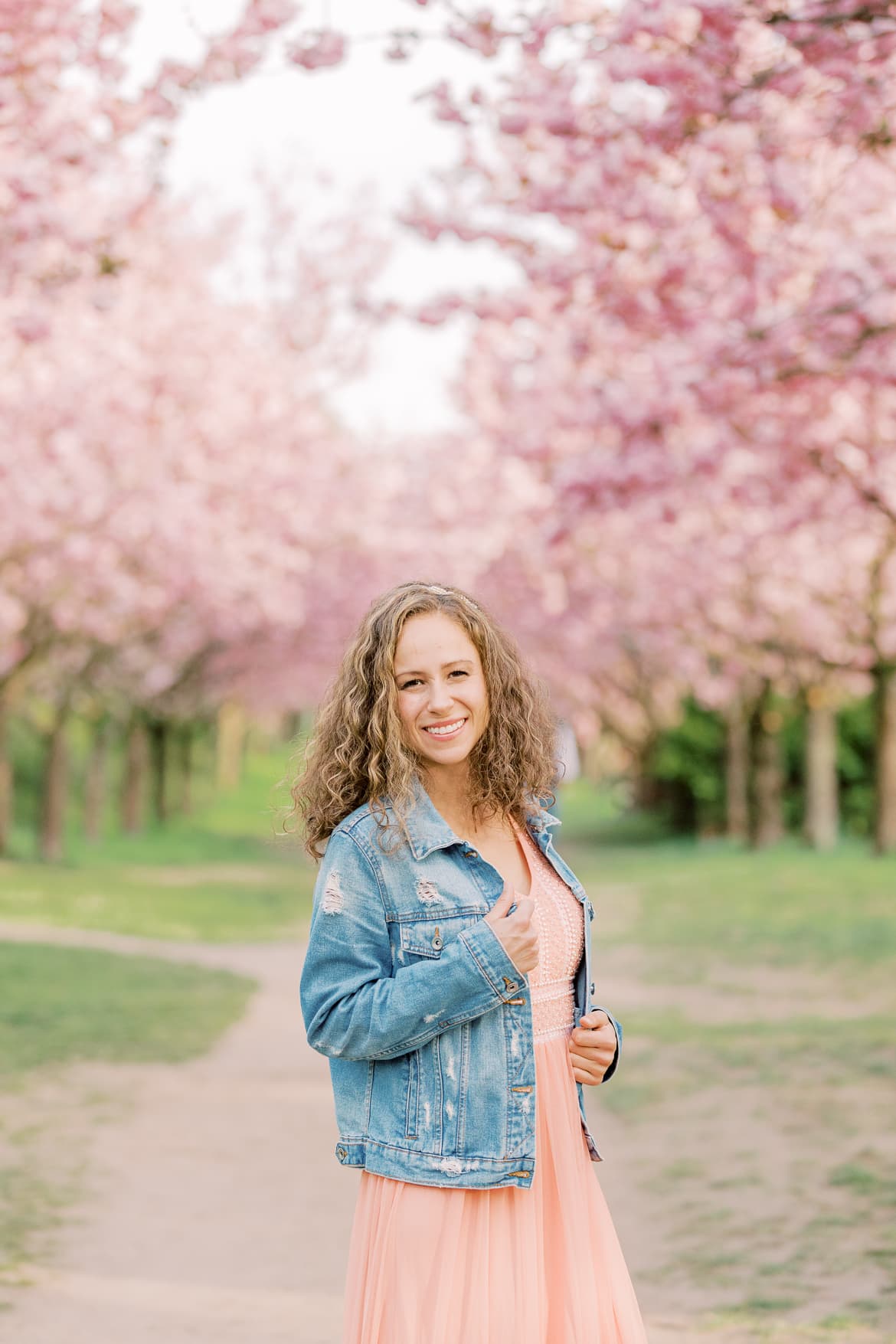 Eine Frau mit Locken, Abendkleid und Jeansjacke unter Kirschblüten