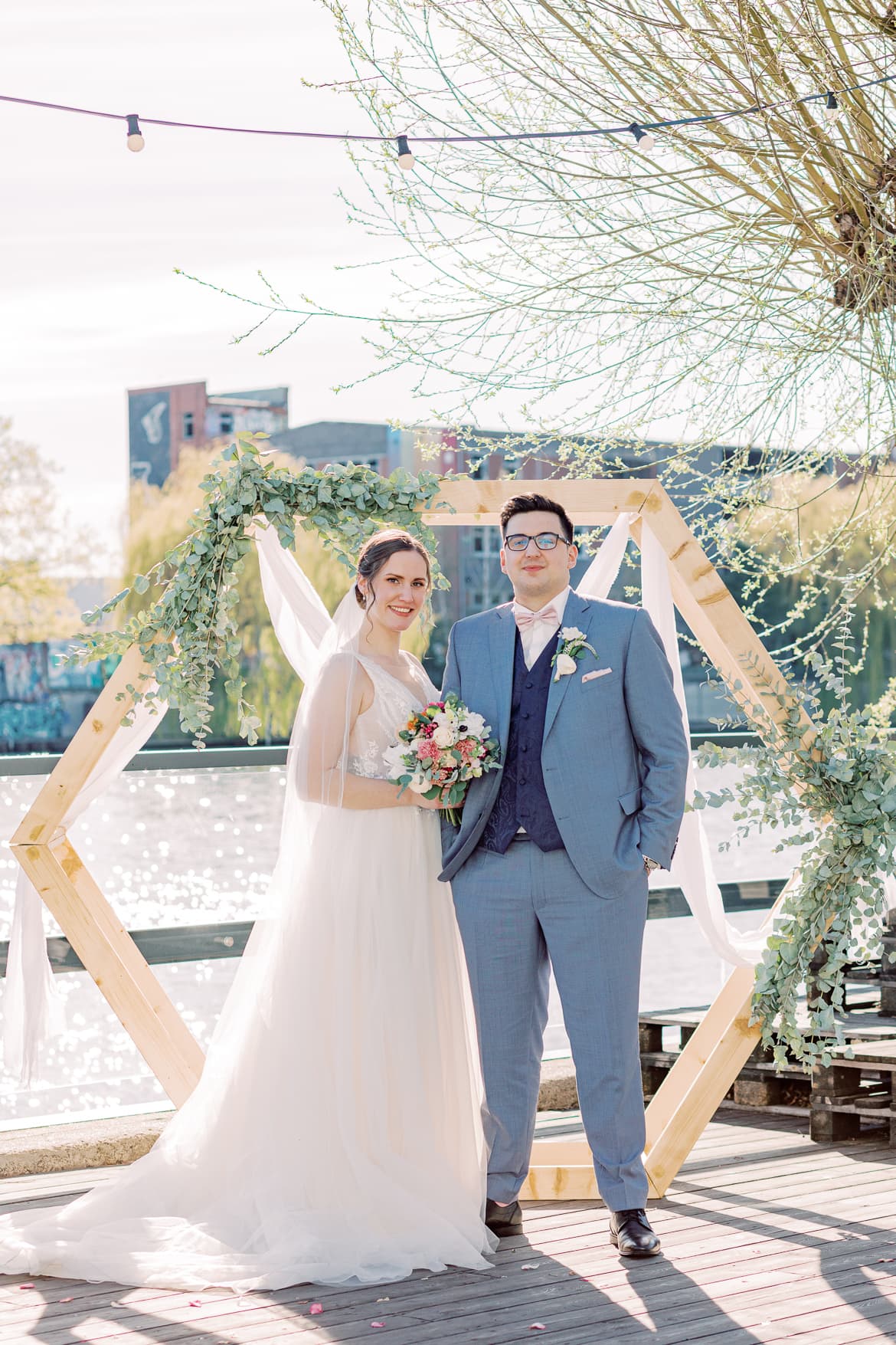 Hochzeitspaar vor einem Traubogen an der Spree