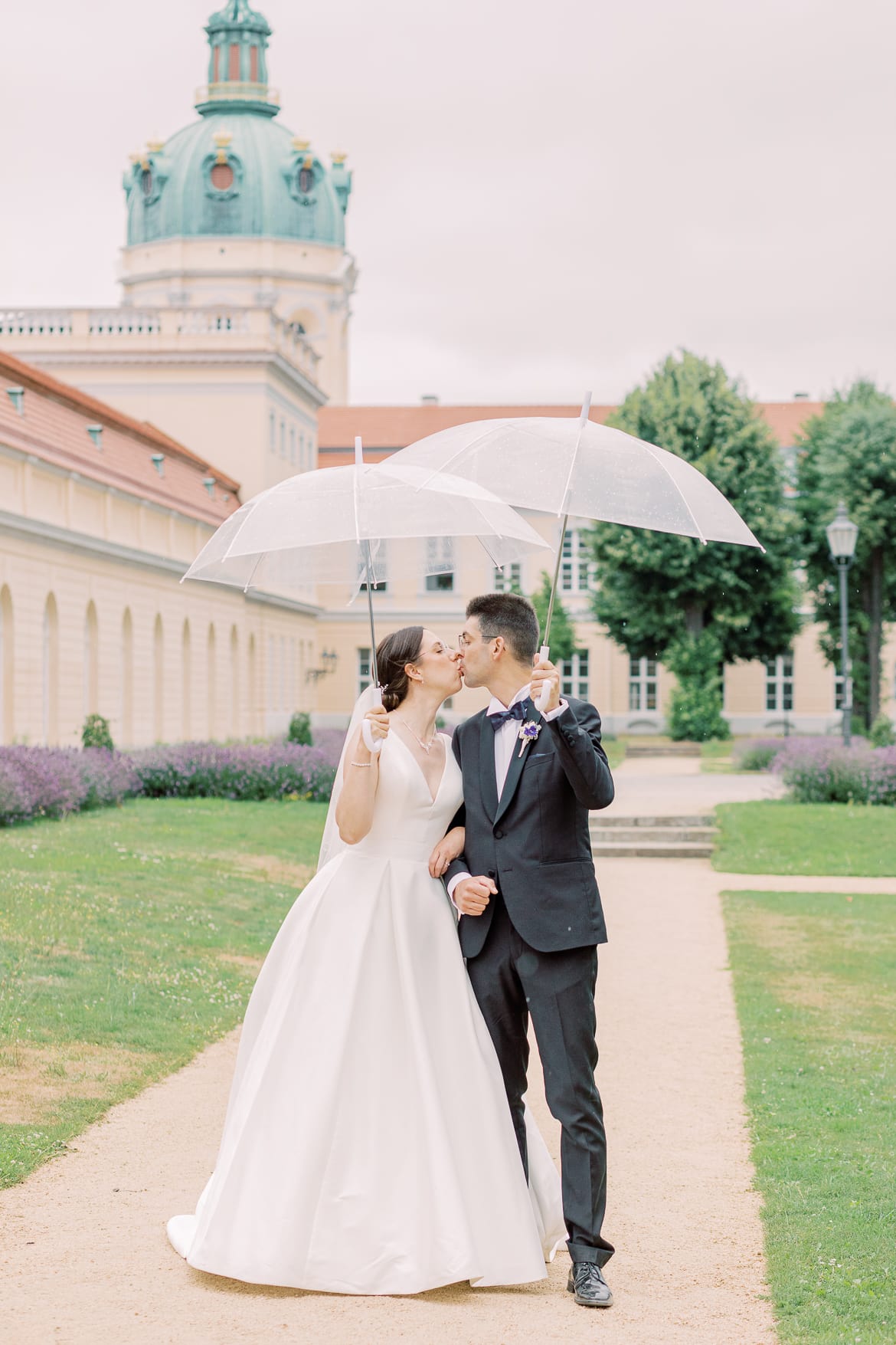 Brautpaar spaziert mit Regenschirmen im Park