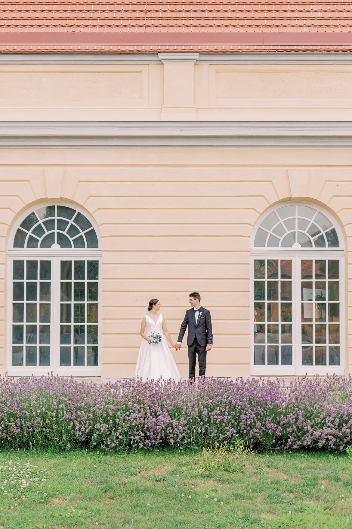 Brautpaar hält sich vor einem Schloss an den Händen