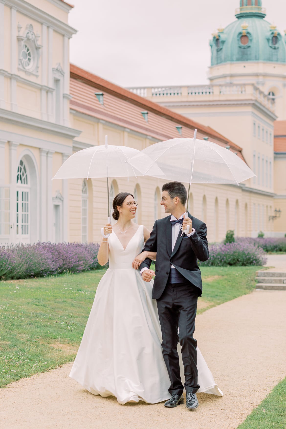 Brautpaar spaziert mit Regenschirmen im Park