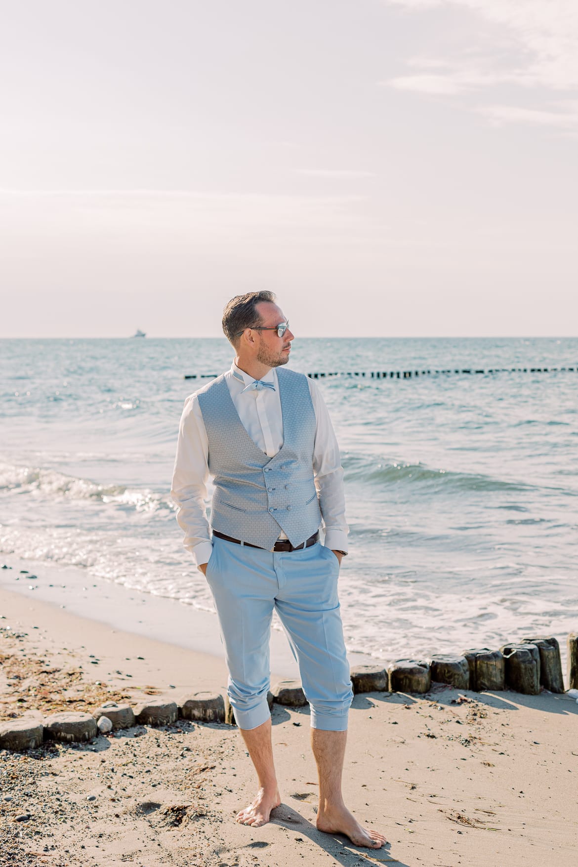 Bräutigam steht am Strand und schaut aufs Meer