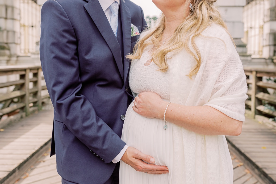 Hochzeitspaar umarmt den Babybauch der Braut