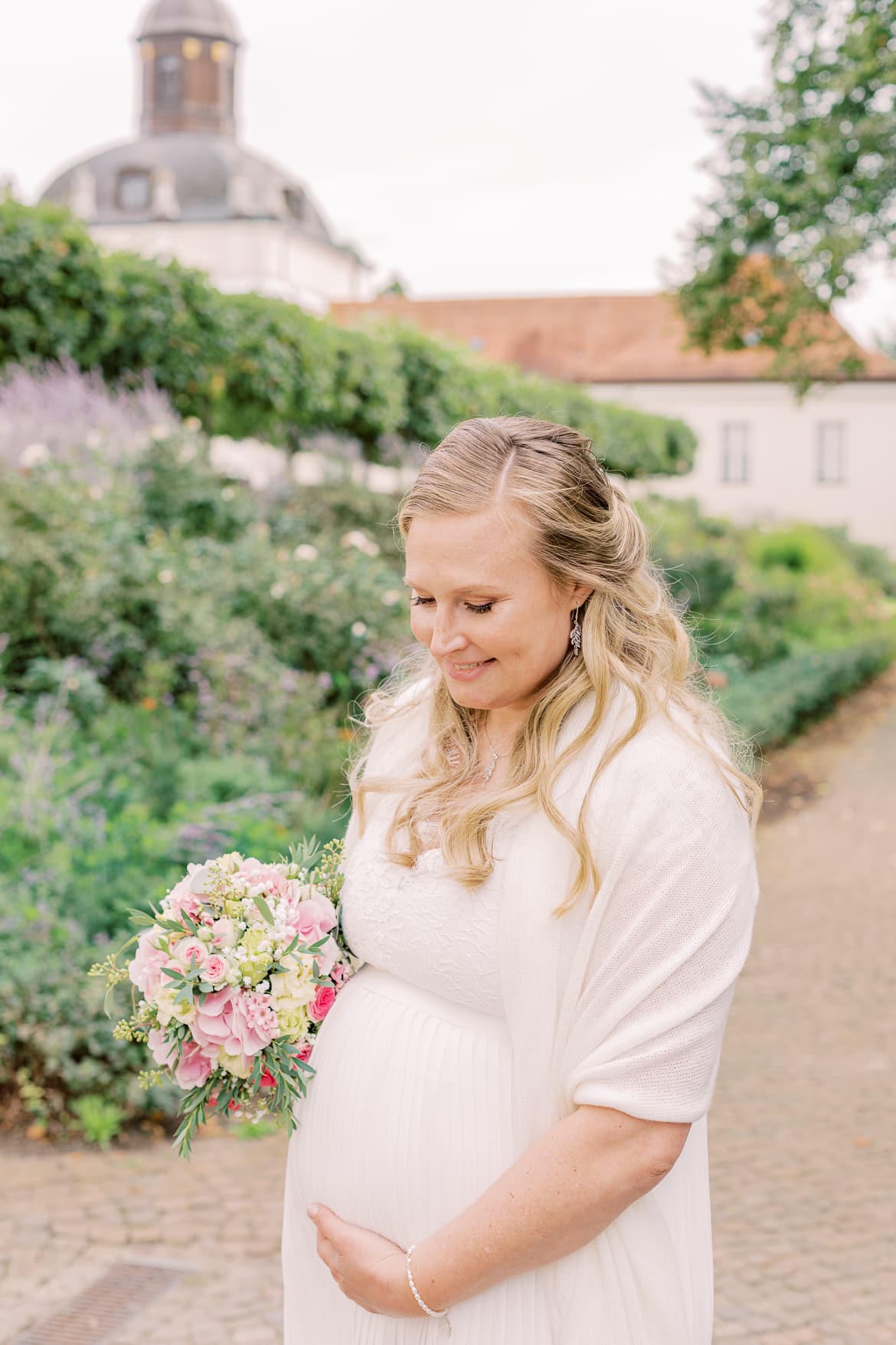 Braut umarmt ihren Babybauch und lächelt