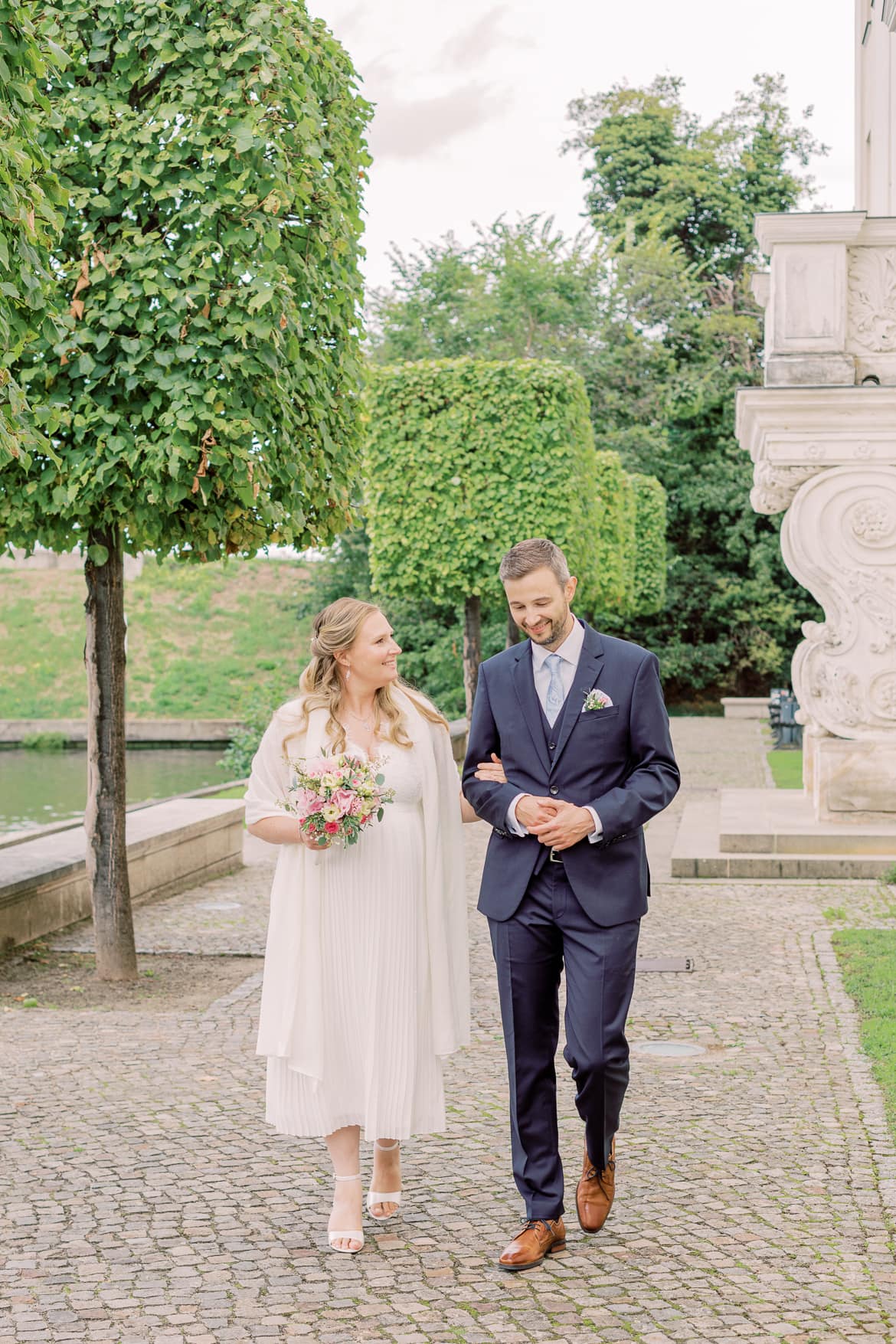 Hochzeitspaar spaziert lachend neben einem Schloss