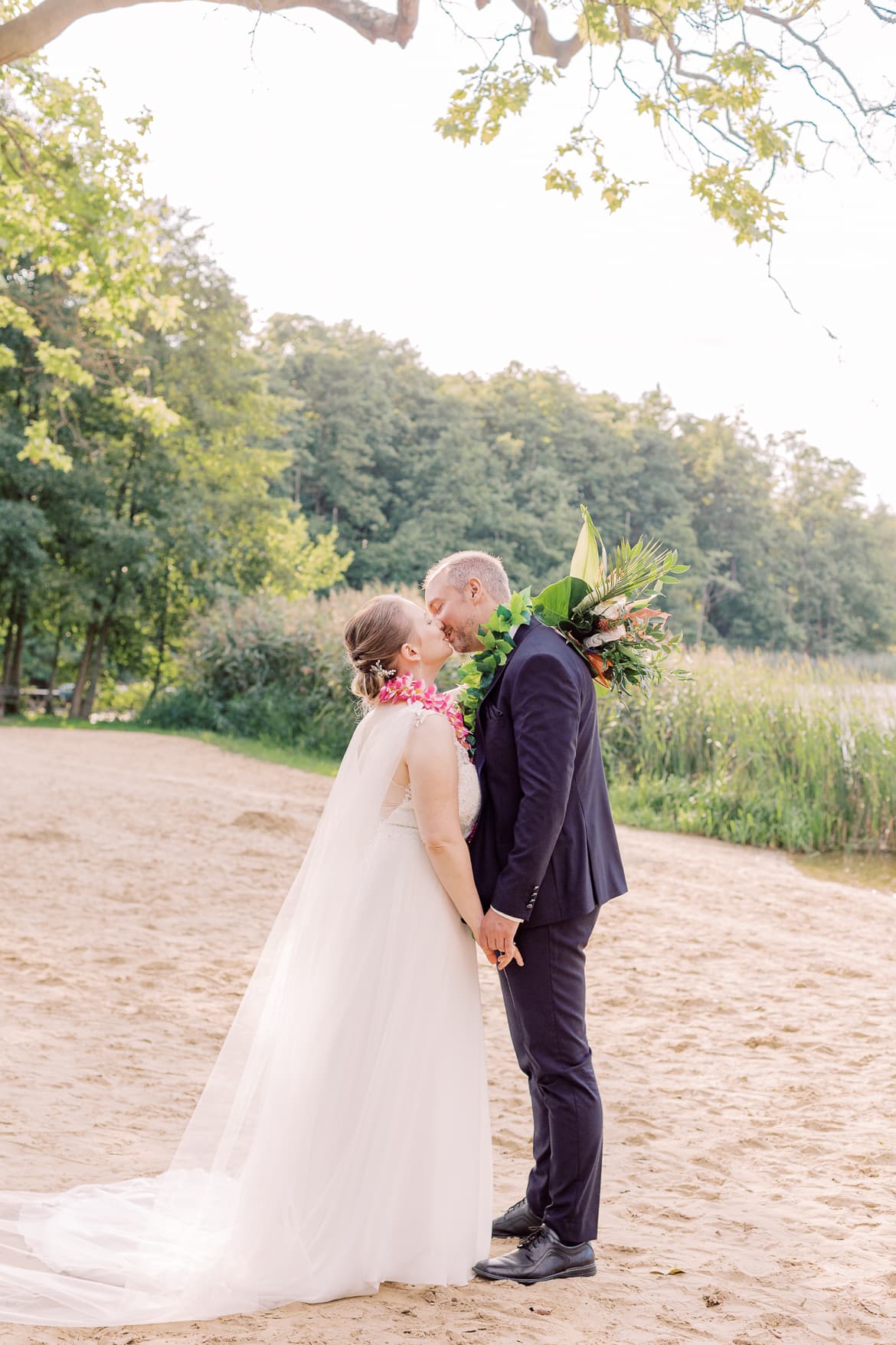 Hochzeitspaar küsst sich am Ufer eines Sees