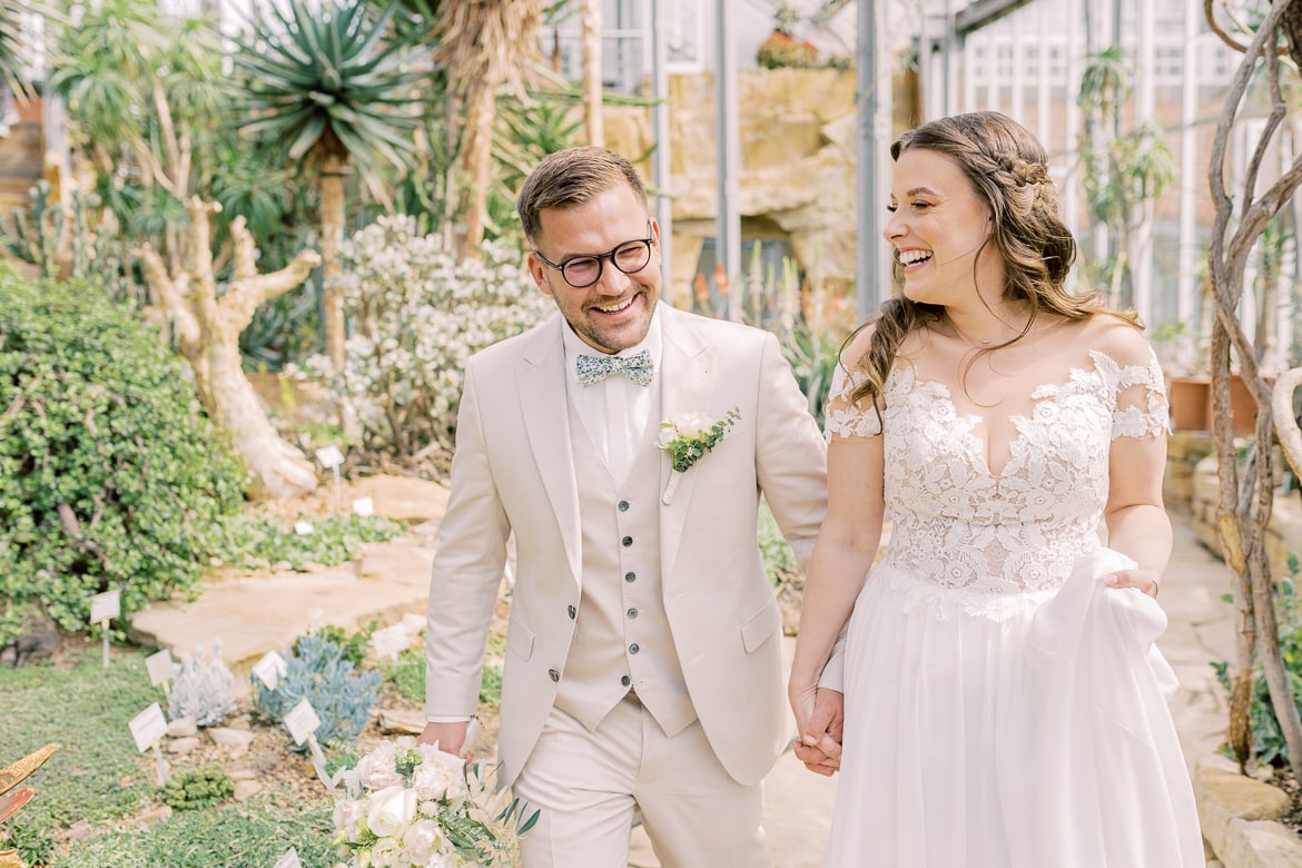 Ein Hochzeitspaar läuft lachend durch ein Gewächshaus im Botanischen Garten Berlin