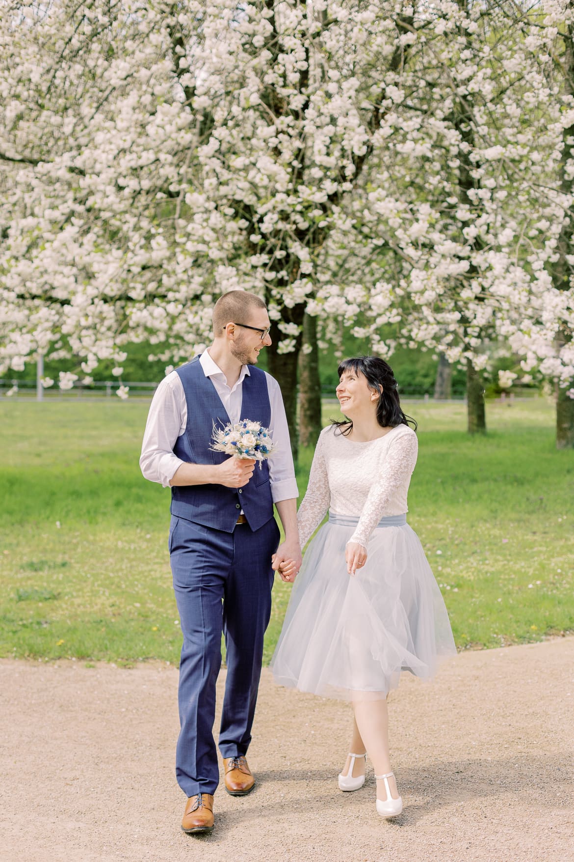 Hochzeitspaar spaziert vor einem blühenden Baum im Park