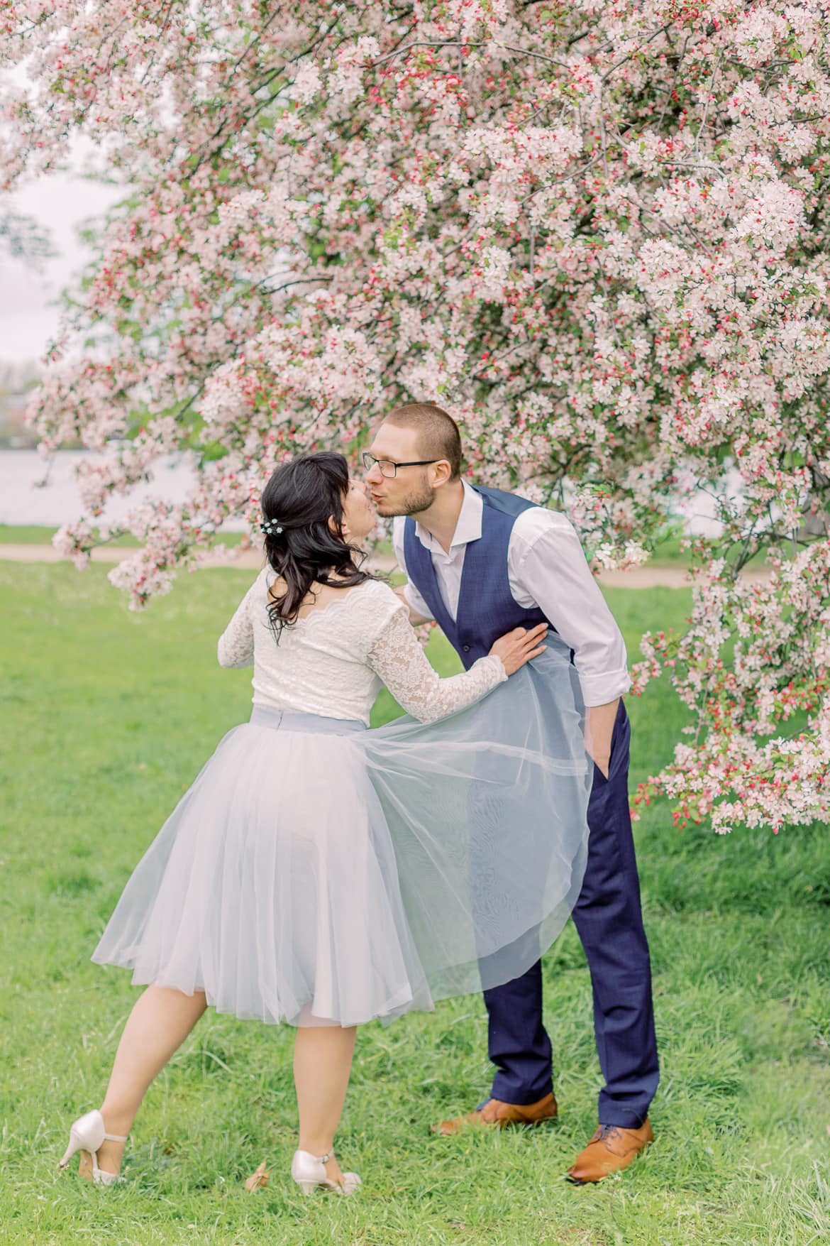 Hochzeitspaar küsst sich vor einem blühenden Baum im Park