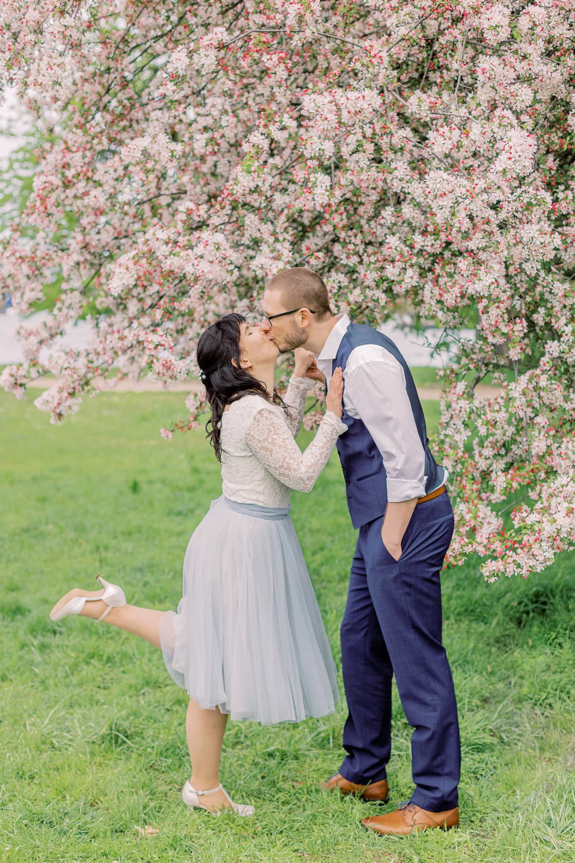 Hochzeitspaar küsst sich vor einem blühenden Baum im Park