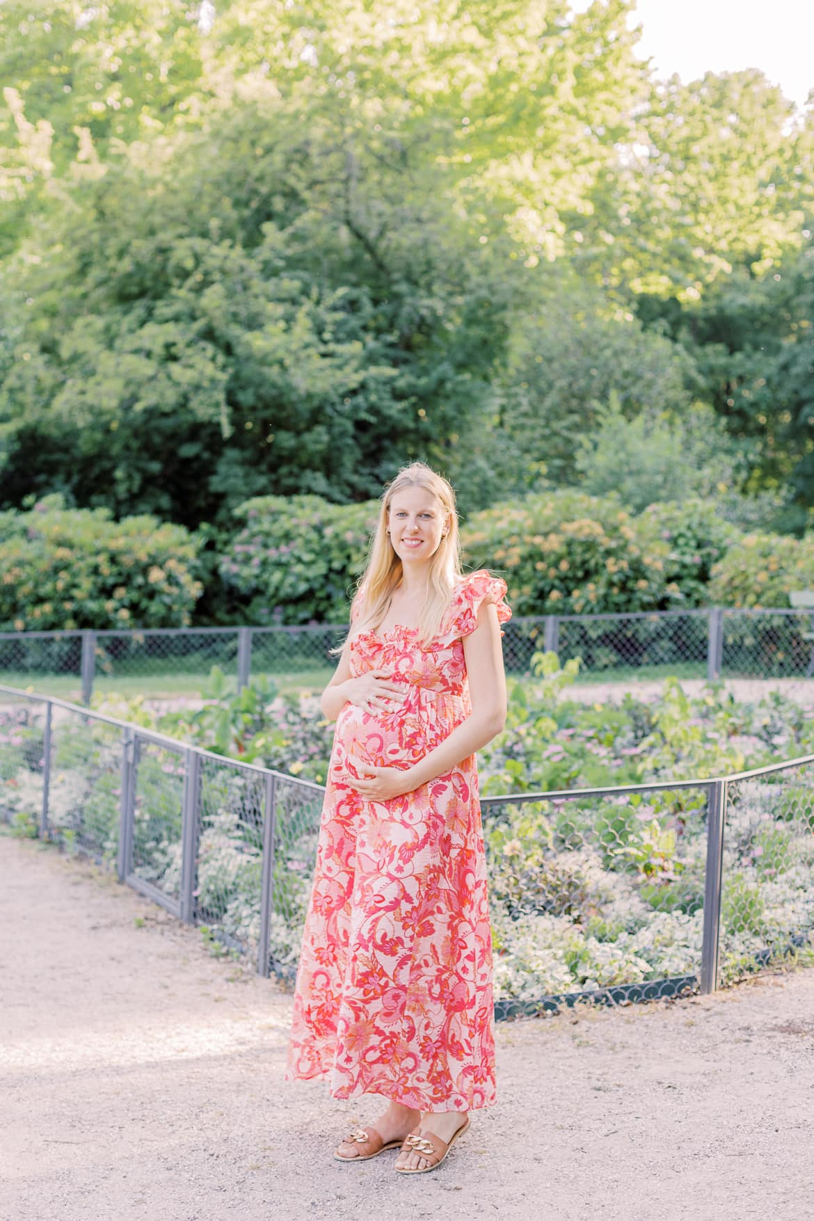 Schwangere Frau lacht in die Kamera und hält ihren Babybauch