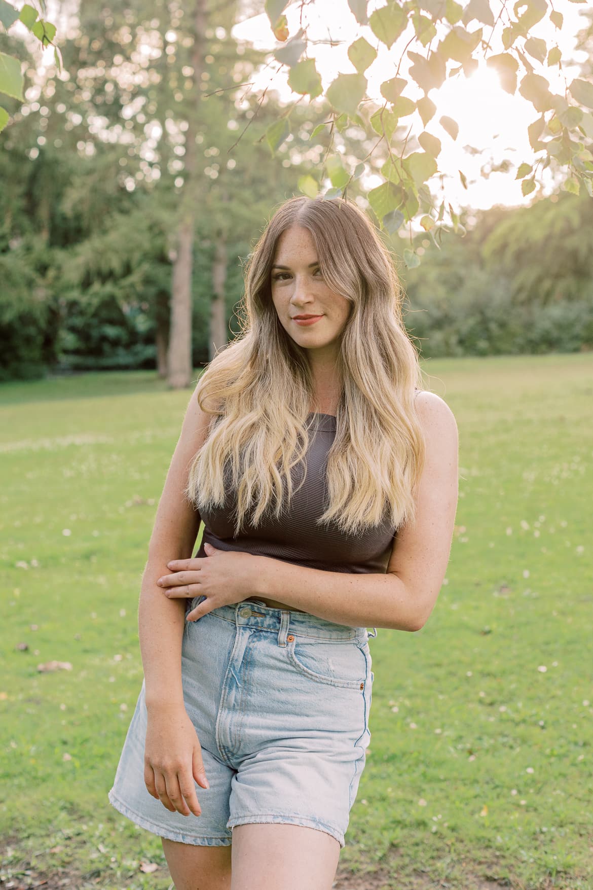 Frau mit blonden Haaren in der Abendsonne im Park schaut in die Kamera