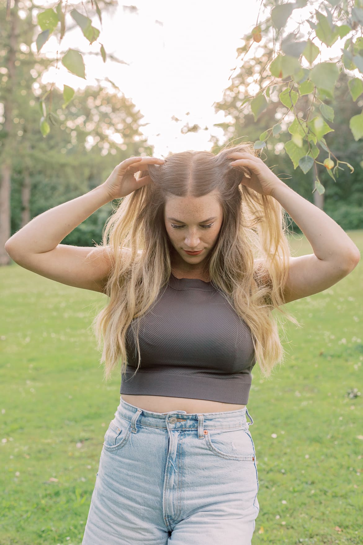 Frau greift sich mit Händen in die blonden Haare in der Abendsonne im Park