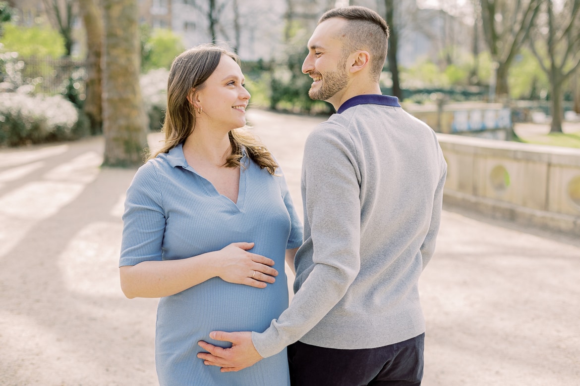 Ein schwangeres Paar steht zusammen und lacht sich an, beide haben ihre Hände auf dem Bauch