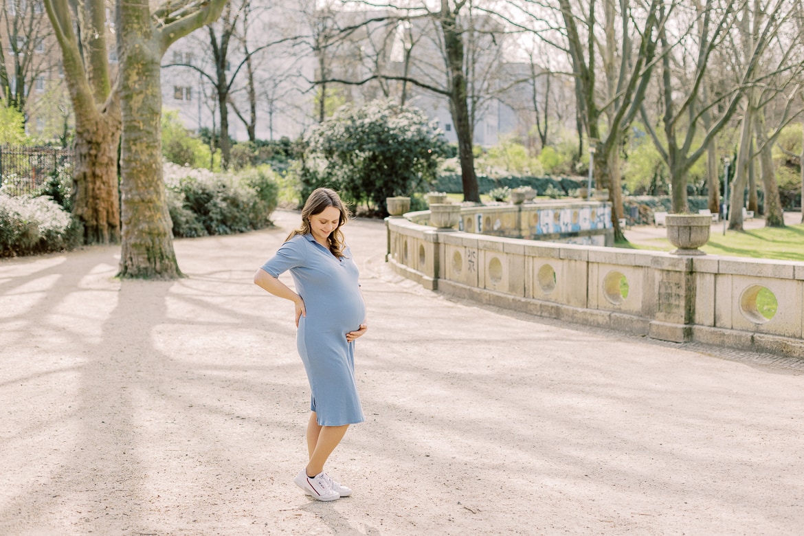 Eine schwangere Frau steht im Park und schaut auf ihren Babybauch