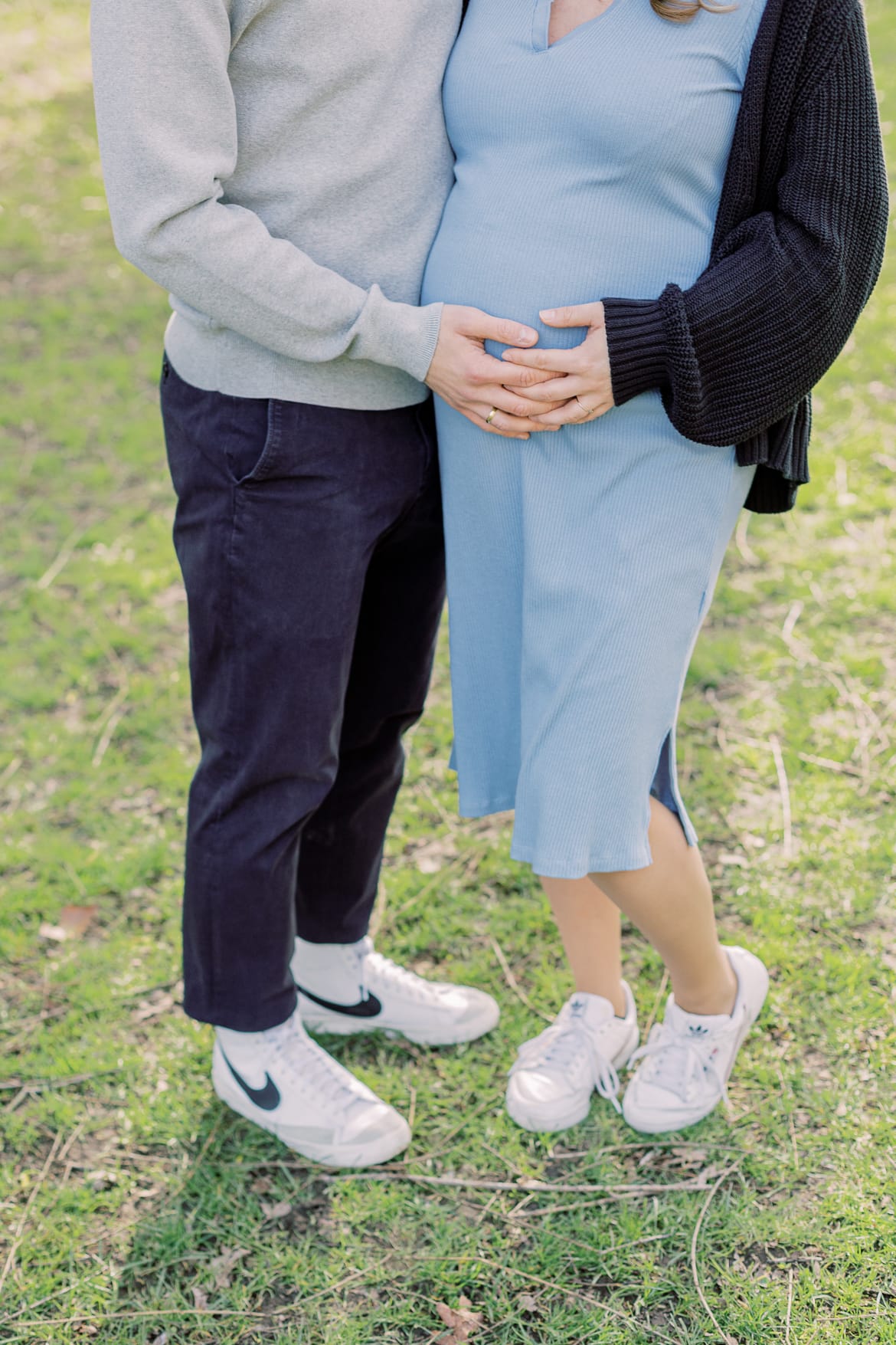 Ein schwangeres Paar steht auf einer Wiese, beide halten den Babybauch