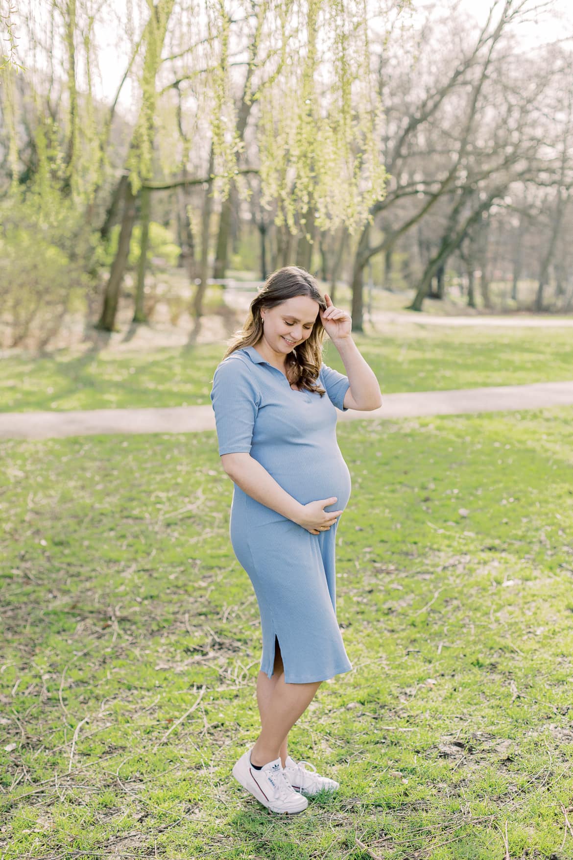 Eine schwangere Frau steht auf einer Wiese und schaut auf ihren Babybauch