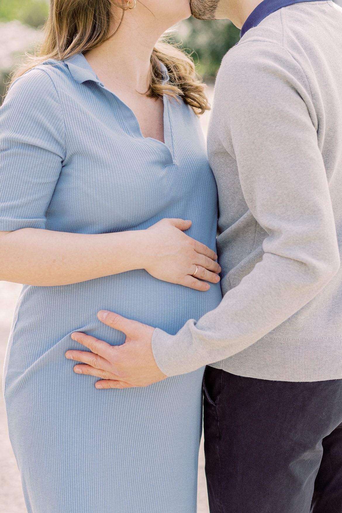 Ein schwangeres Paar küsst sich und beide halten ihre Hände auf dem Bauch