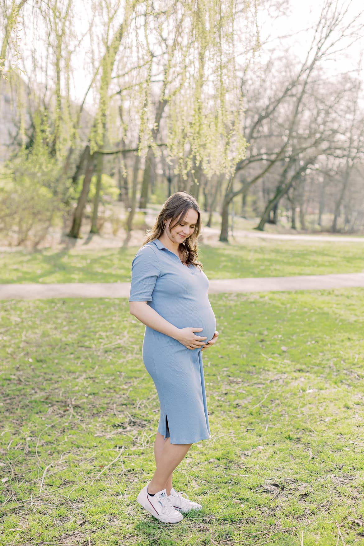 Eine schwangere Frau steht auf einer Wiese und schaut auf ihren Babybauch